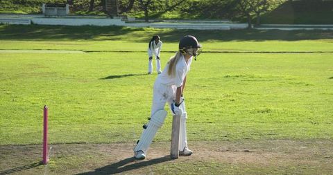 Female cricketer batting on sunny green pitch