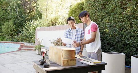 Father and son building wooden box on patio with plans in hand