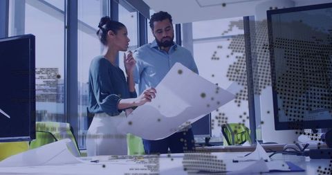 Coworkers reviewing blueprint with digital overlay in modern office collaborating on design planning