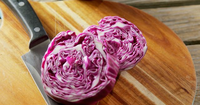 Freshly sliced purple cabbage on a wooden cutting board with a kitchen knife beside it. Ideal for use in culinary blogs, healthy eating guides, dietary nutrition content, vegan and vegetarian cooking recipes.
