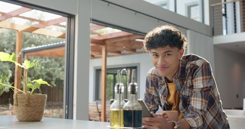 Young Man Relaxing in Modern Kitchen with Smartphone and Coffee