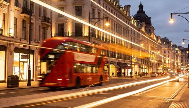 Red double-decker bus creating streaking light trails on historic london shopping street