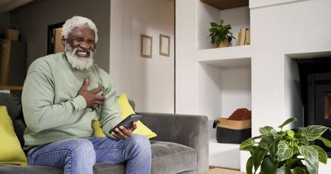 Senior man experiencing discomfort at home with smartphone