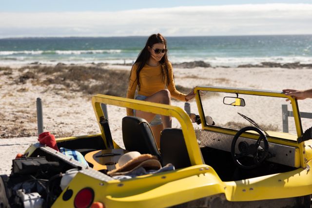 Smiling caucasian woman climbing into beach buggy on sunny beach by the sea. beach stop off on summer holiday road trip.