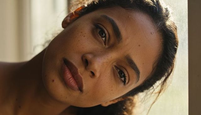 Sunlit natural light closeup of freckled woman leaning by window with bare shoulder