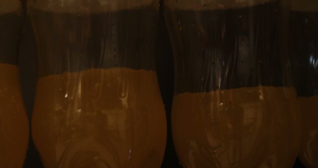 This image can be used for advertising bars, pubs, and breweries. It is ideal for emphasizing the refreshment and appeal of beer. This close-up conveys the intricacies of the condensation and lighting, highlighting the contrast between dark and golden colors. Perfect for use in promotional materials, social media posts, and websites related to nightlife and beverage industry.