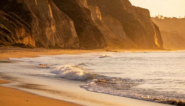 Golden sunset waves lapping along rugged coastal cliffs, wet sand glowing in warm light