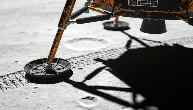 Lunar lander leg casting sharp shadow on moon regolith, circular footpad and gold foil
