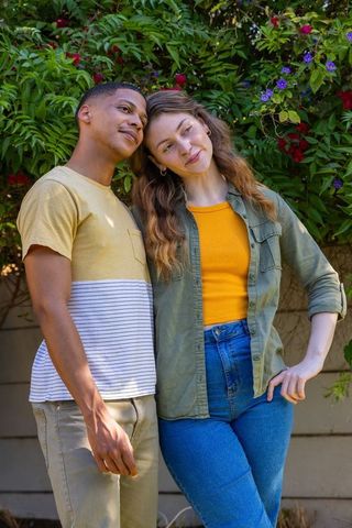 Young couple leaning in garden with flowering vines wearing casual colorful outfits