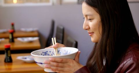 Woman eating noodles with chopsticks in cozy restaurant