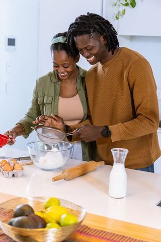 African american couple baking together in modern kitchen sifting flour smiling