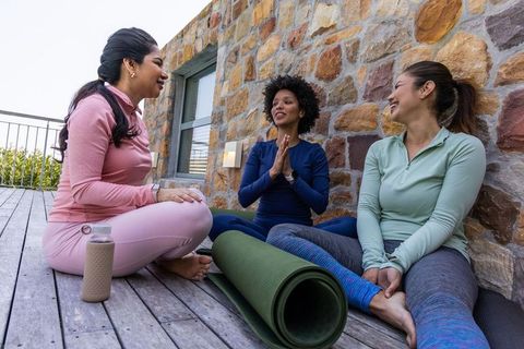 Diverse women practicing yoga and chatting on outdoor deck with reusable water bottle