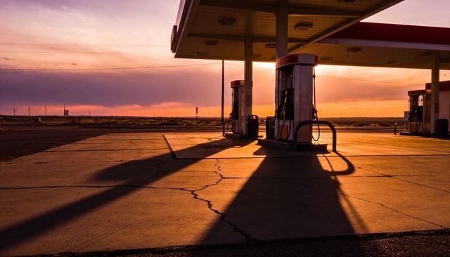 Desert fuel pumps at sunset casting long shadows across cracked concrete canopy