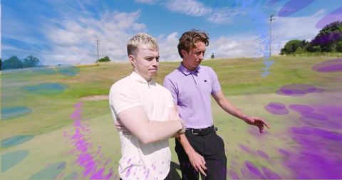 Two men conversing on sunlit golf green wearing cream and lavender polo shirts