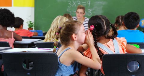 Schoolgirl whispering to friend during class activity