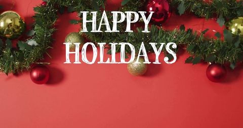 Happy holidays typography with fir garland and gold red baubles on red field