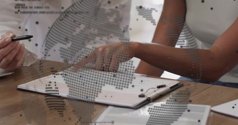 Female team collaborating over documents with global map overlay in modern office