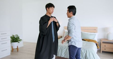 Father adjusting son's graduation gown for ceremony celebration
