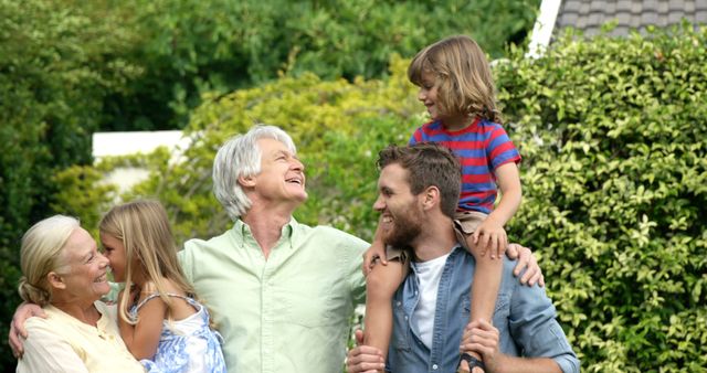 This image shows a multi-generational family enjoying time together in a lush green garden. Grandparents, parents, and children are smiling and interacting warmly with each other, highlighting the theme of family bonding and happiness. This picture is perfect for usage in family-focused advertisements, community event promotions, lifestyle blogs, or any content celebrating family relationships and outdoor activities.