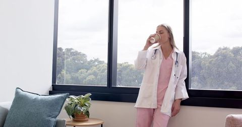 Female doctor taking coffee break by window in calm clinic lounge with natural view