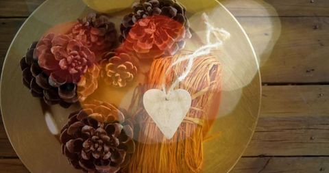 Displaying golden bowl with pine cones and heart tag, rustic autumn decor with warm bokeh glow