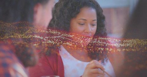 Woman enjoying casual dinner in red cardigan with golden bokeh, intimate meal