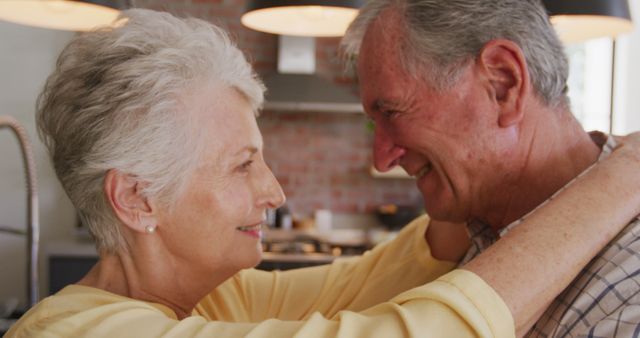 Happy senior caucasian couple smiling at each other and embracing in kitchen. Romance, love, senior lifestyle and togetherness.