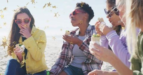 Friends Enjoying Wraps on Sunny Beach Wearing Colorful Jackets and Retro Sunglasses
