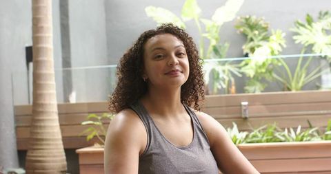 Confident african american woman sitting on patio bench smiling in gray tank top