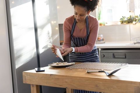African american woman decorating cookies with piping bag at sunlit kitchen island