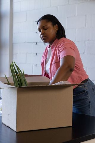 African american woman packing plant into cardboard box with bubble wrap at small business workspace