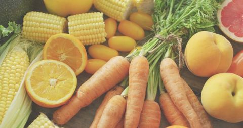 Showcasing fresh harvest spread of carrots, corn, citrus and stone fruit on rustic wood