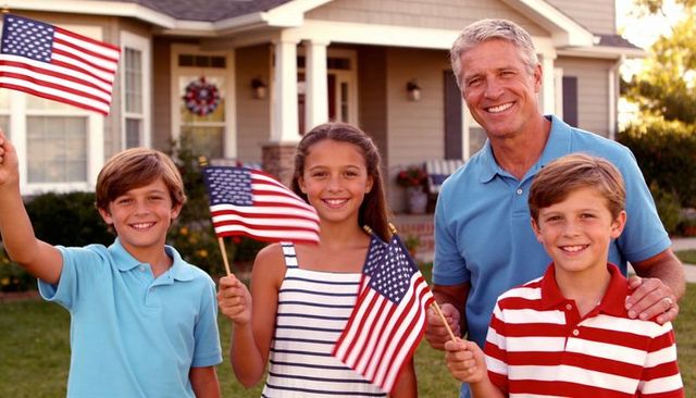 Smiling grandfather and children waving american flags on porch celebrating patriotic family moment