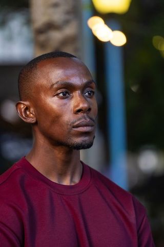 African american man gazing upward at dusk with warm bokeh lights wearing burgundy shirt