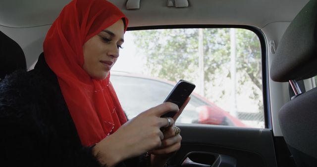 Muslim woman checks her phone in a car, with copy space. She appears engaged with her device, during a commute or travel.