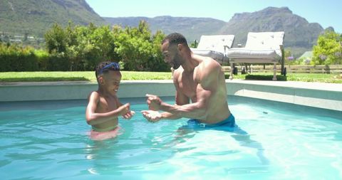 African american father teaching son to swim in backyard pool, sunny family summer fun