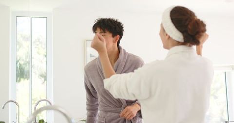 Diverse couple grooming together at bright minimalist bathroom vanity in robes