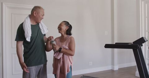 Happy elderly couple bonding after home workout with treadmill