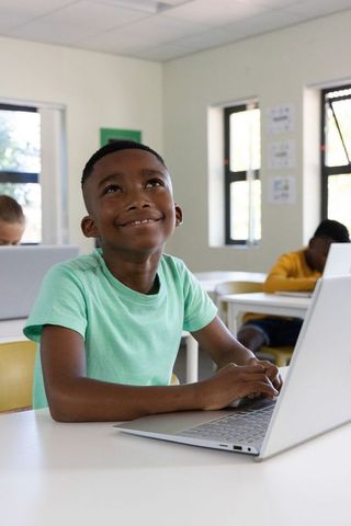 African american boy typing on laptop in classroom, smiling and imagining future success