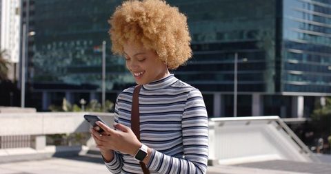 Young woman checking smartphone and wearing smartwatch in modern urban plaza