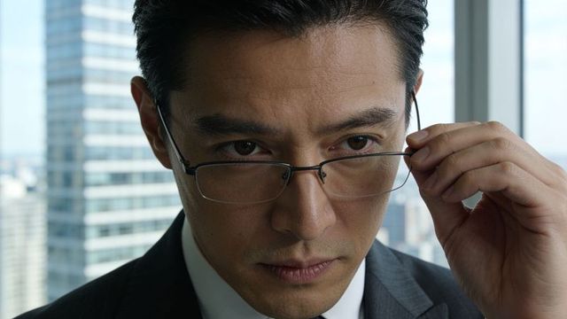 Asian executive adjusting glasses in high-rise office conveying focus and corporate leadership