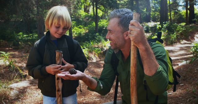 Father and son bonding while hiking in lush forest, man showing boy a pine cone. Perfect for content about family outdoor activities, nature exploration, relationships, adventure travel, and childhood education.