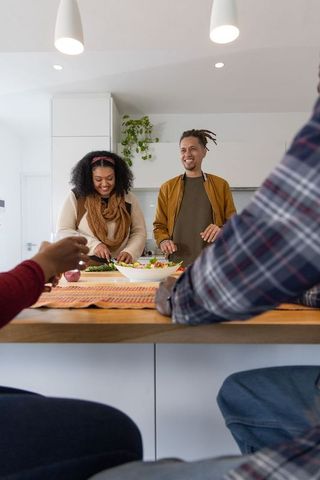 Diverse friends preparing fresh salad at kitchen island laughing while cooking together