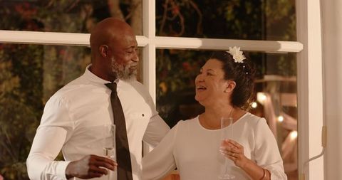 Elderly diverse couple celebrating with champagne in warm garden setting