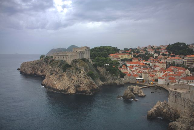 Panoramic view of a historic coastal town featuring a cliffside fortress and numerous red-tiled rooftops beside the clear blue water of the Adriatic Sea. Ideal for use in travel brochures, heritage site promotions, or historical documentaries highlighting Europe's medieval architecture and scenic destinations.