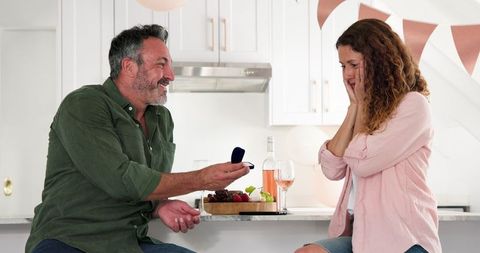Man proposing to joyful woman with engagement ring at home celebration