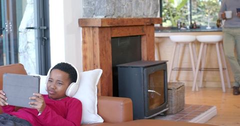 African american father and son relaxing in cozy open-plan living room, child using tablet