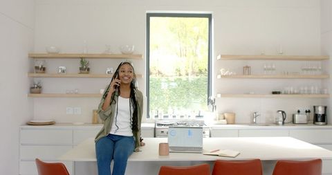 Young Woman with Braids Smiling While On Phone in Modern Kitchen