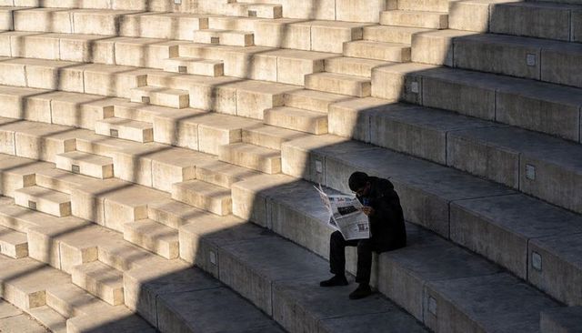 Solitary Man Reading Newspaper on Concrete Steps with Dramatic Diagonal Shadows