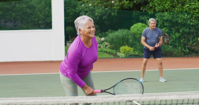 Image of happy biracial senior couple during training on tennis court. active retirement lifestyle, senior relationship and tennis training concept.